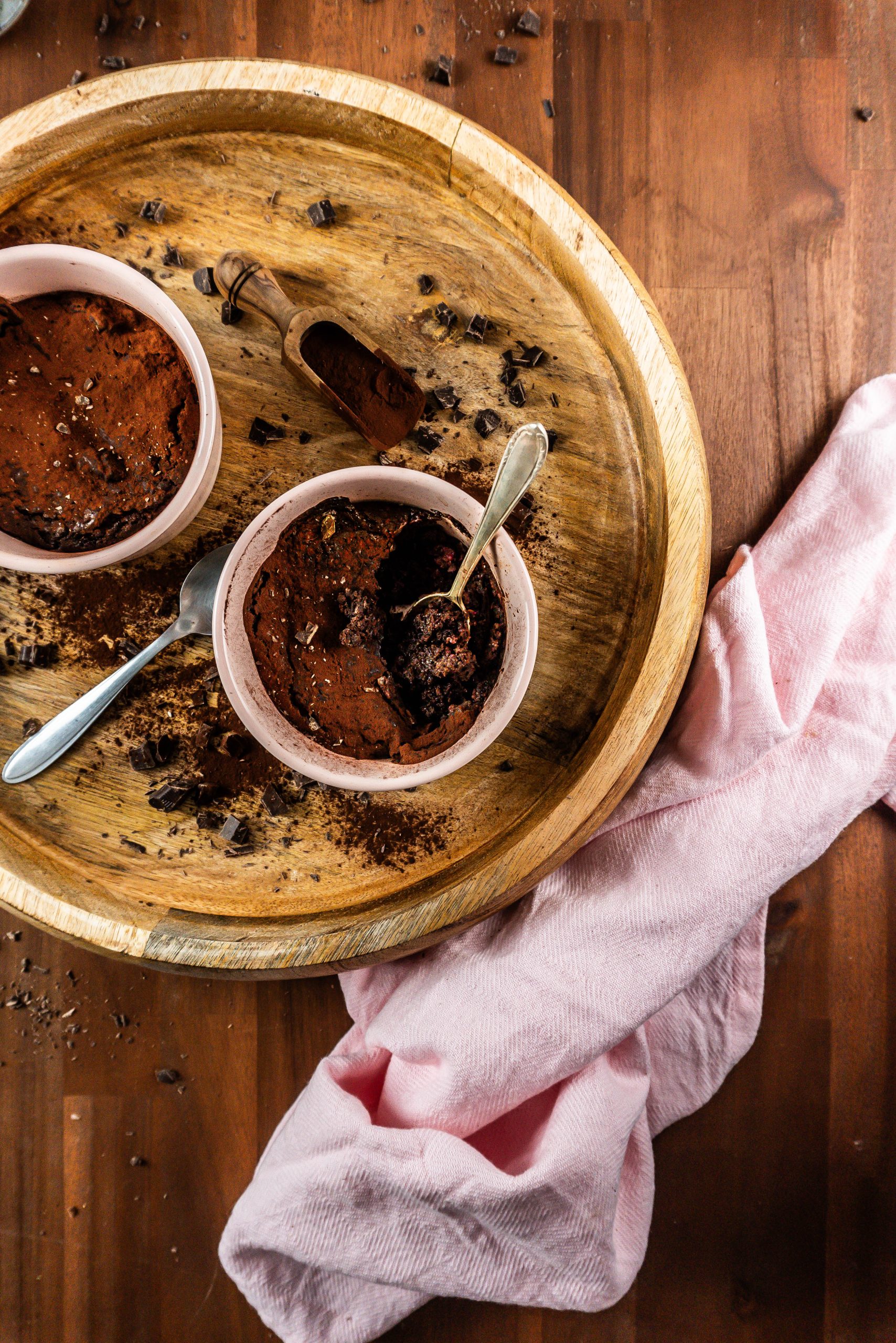 Gluten-free warm, fudgy mug brownie in in an oven-proof ramekin with a spoon tugged into it and it being half eaten surrounded with chopped chocolate and cocoa powder