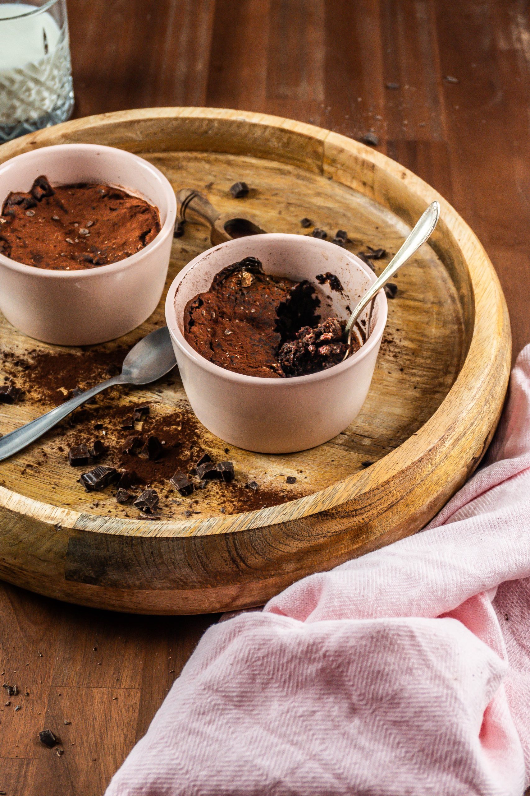 Gluten-free warm, fudgy mug brownie in in an oven-proof ramekin with a spoon tugged into it and it being half eaten surrounded with chopped chocolate and cocoa powder