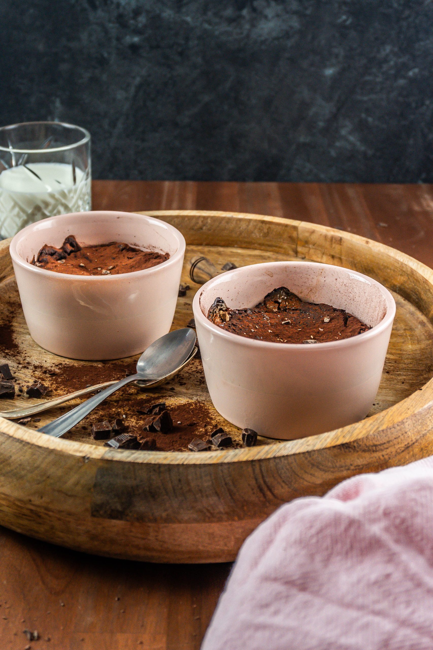 Gluten-free warm, fudgy mug brownies in in an oven-proof ramekin surrounded with chopped chocolate and cocoa powder; photographed from a side angle