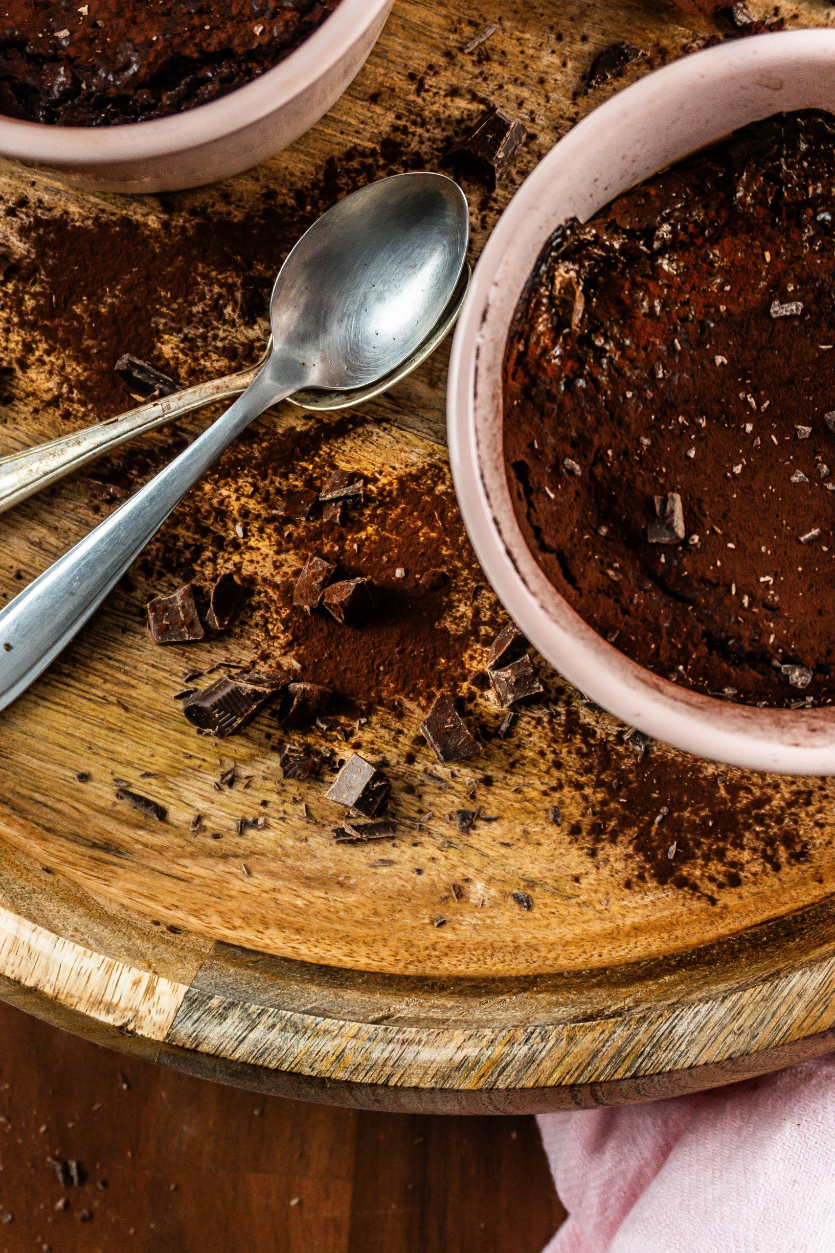 Chopped chocolate and cocoa powder on a wooden tray surrounded with spoons and gluten-free warm, fudgy mug brownies