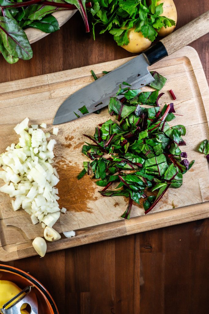 Swiss chard being cut next to an already finely chopped onion