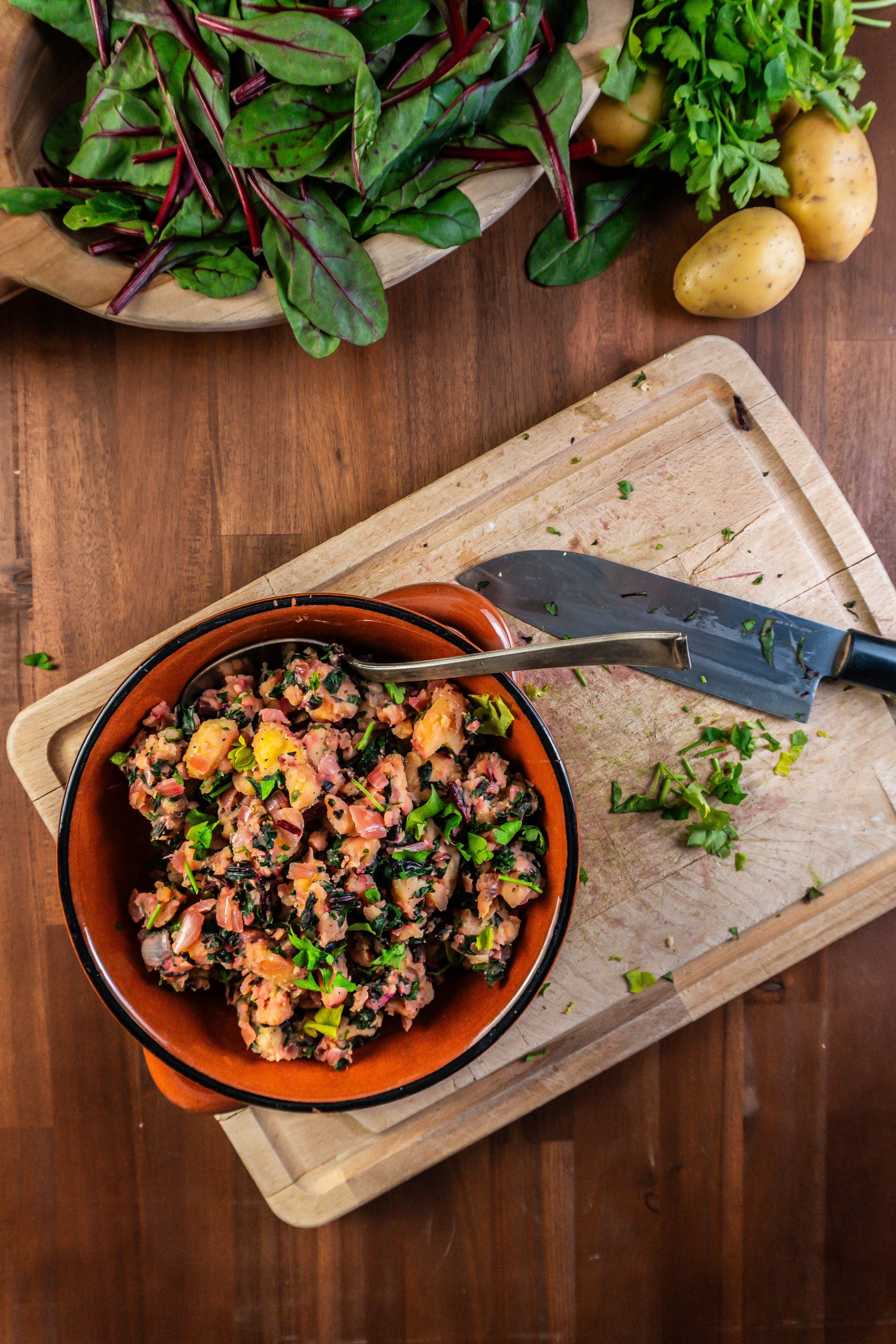 Blitva - Croatian Swiss Chard and Potatoes in a brown bowl with a spoon stuck into it; photographed from above