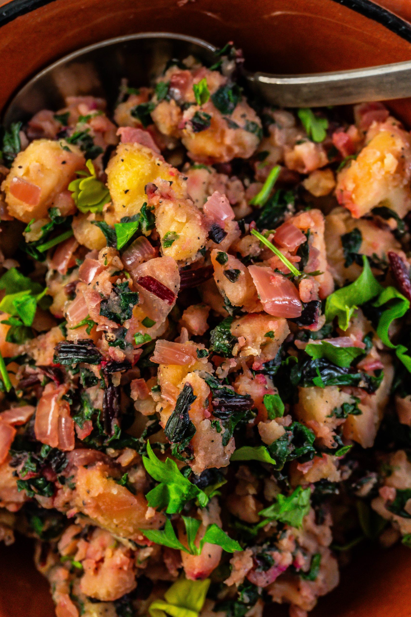 Blitva - Croatian Swiss Chard and Potatoes in a brown bowl with a spoon stuck into it; photographed up close