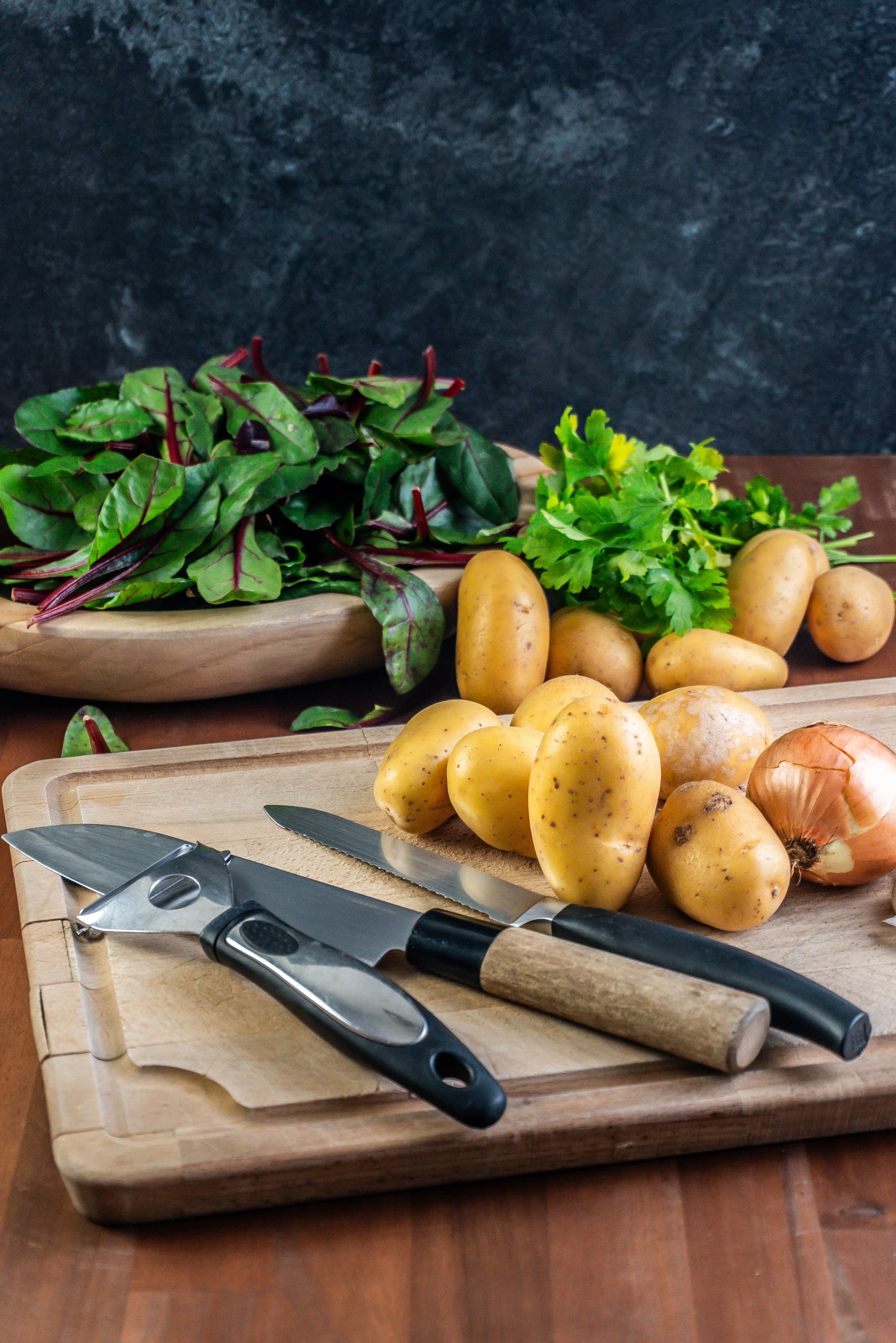 Potatoes and an onion lying on a chopping board, ready for peeling