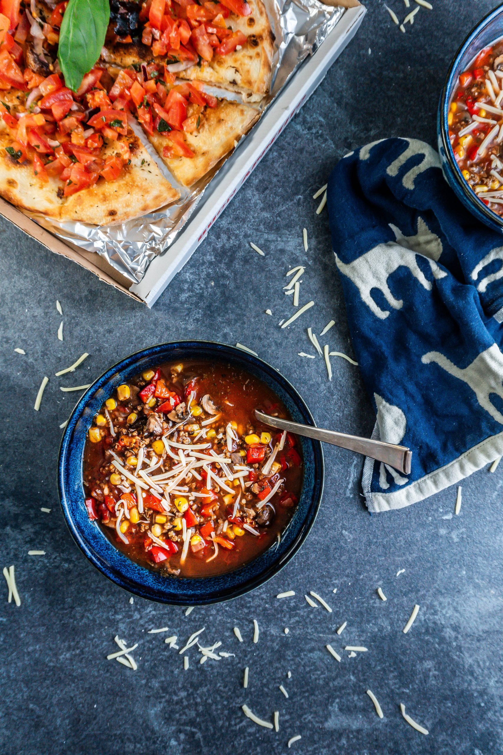 Hearty Vegan Pizza Soup Bowl decorated with some cheese and spoon stuck into the bowl