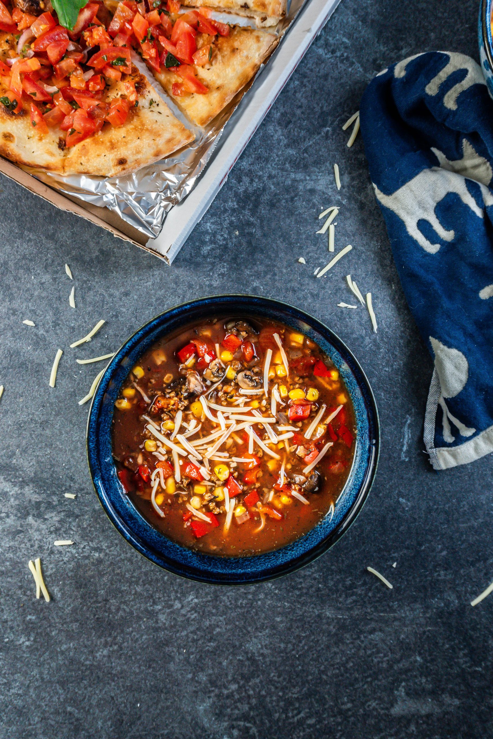 Hearty Vegan Pizza Soup Bowl decorated with some cheese and a pizza bread visible in the background