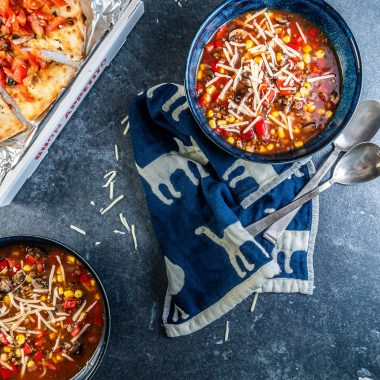 Hearty Vegan Pizza Soup Bowl in two bowls decorated with some cheese and 2 spoons lying on the side
