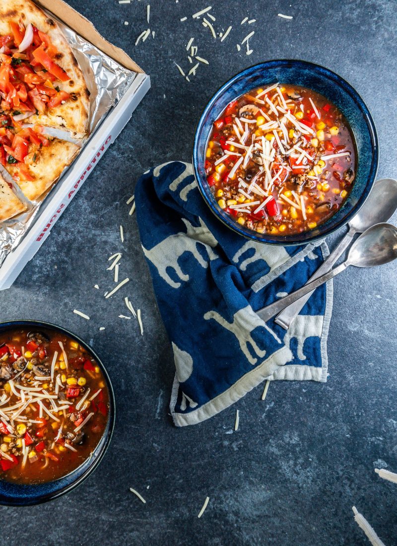 Hearty Vegan Pizza Soup Bowl in two bowls decorated with some cheese and 2 spoons lying on the side