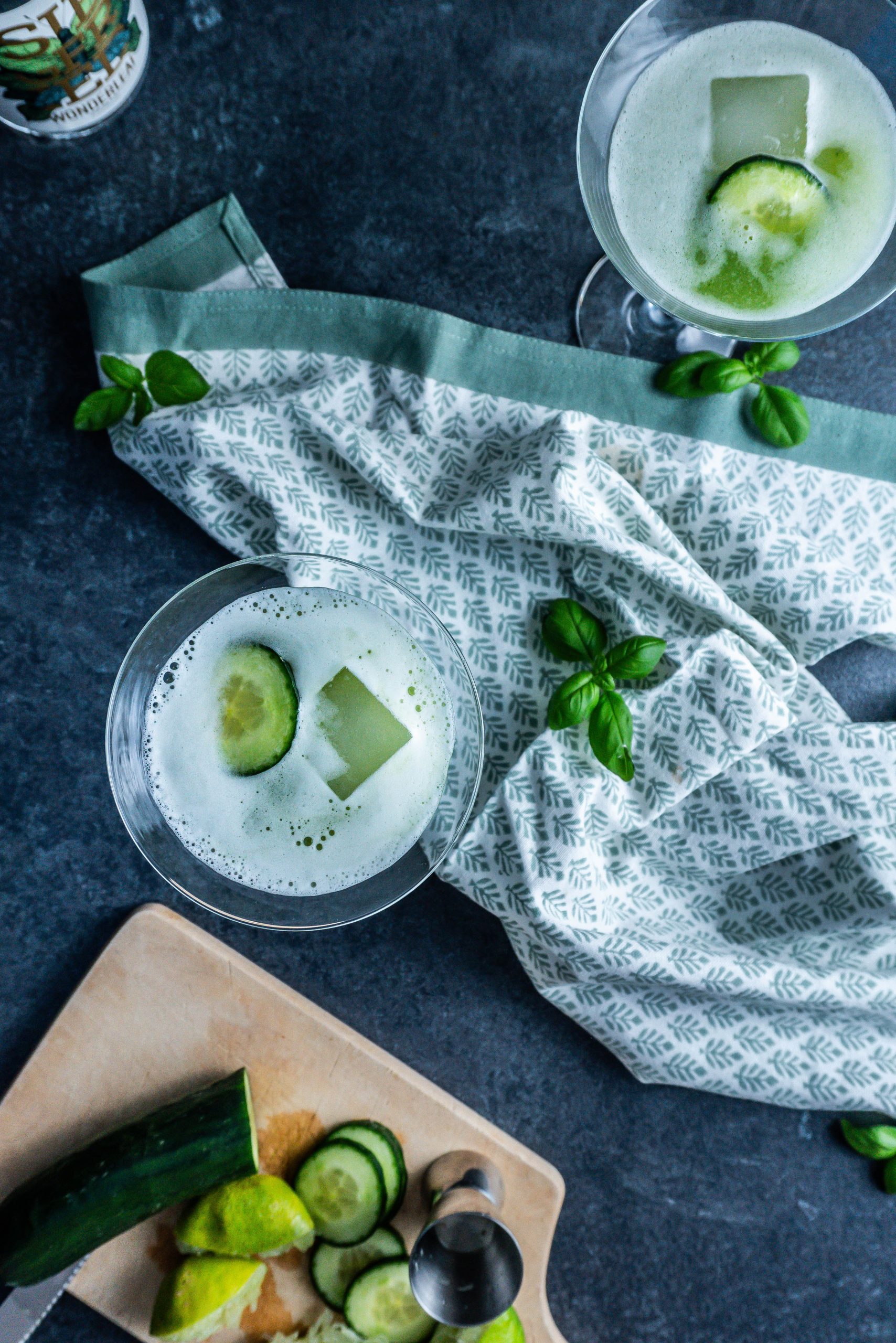 Two non-alcoholic Garden Sour Cocktails in glasses with cucumber slices and juiced limes to the side; photographed from above