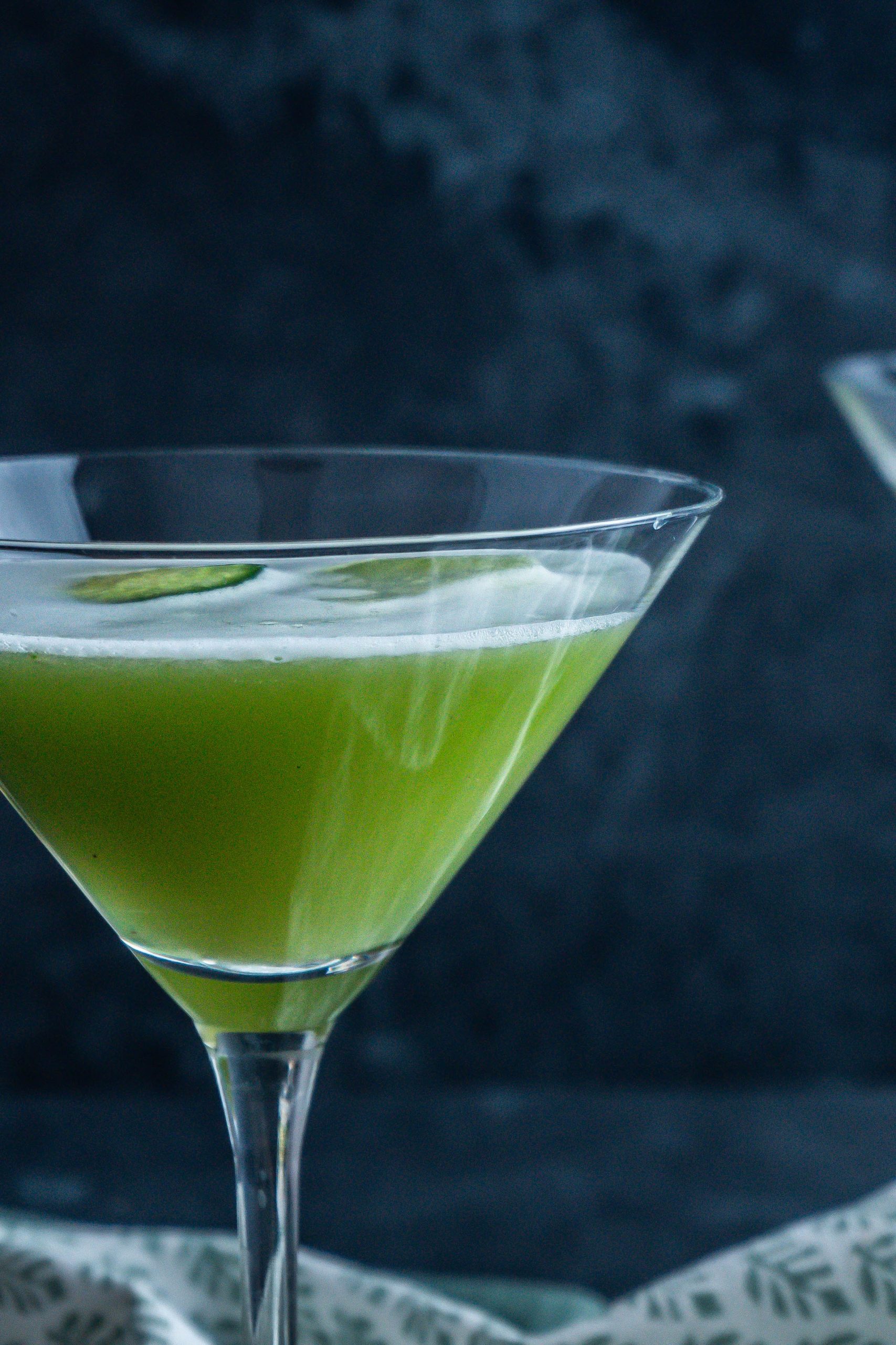 Non-alcoholic Garden Sour Cocktail photographed up close with an ice cube and cucumber slide visible