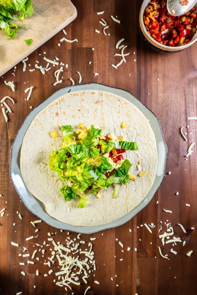 Wrap with fried onion and red peppers, scrambled eggs, crunched nachos, and salad surrounded by other ingredients for the 15-Minute Vegetarian Lunch Crunch Wrap