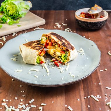 15-Minute Vegetarian Lunch Crunch Wrap, cut in the middle on a plate with some cheese sprinkled around and other ingredients visible in the picture