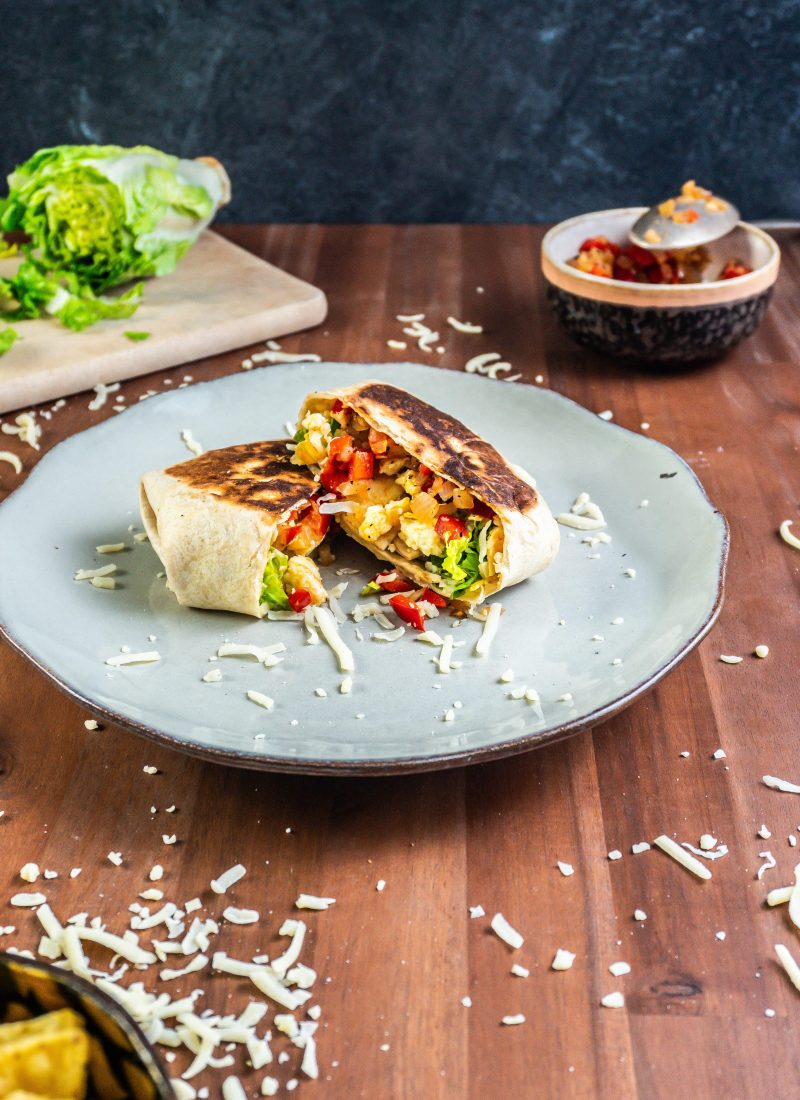 15-Minute Vegetarian Lunch Crunch Wrap, cut in the middle on a plate with some cheese sprinkled around and other ingredients visible in the picture