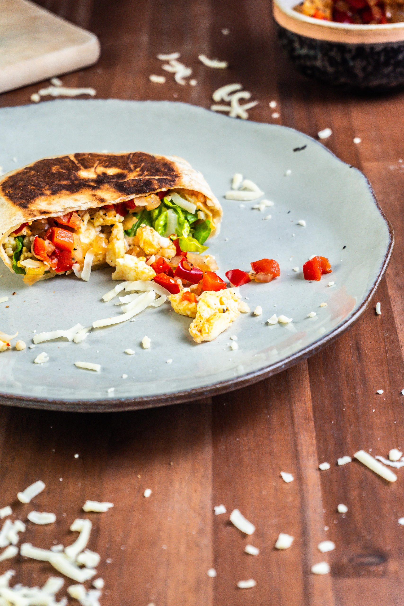 One half of a 15-Minute Vegetarian Lunch Crunch Wrap, cut in the middle on a plate with some cheese sprinkled around