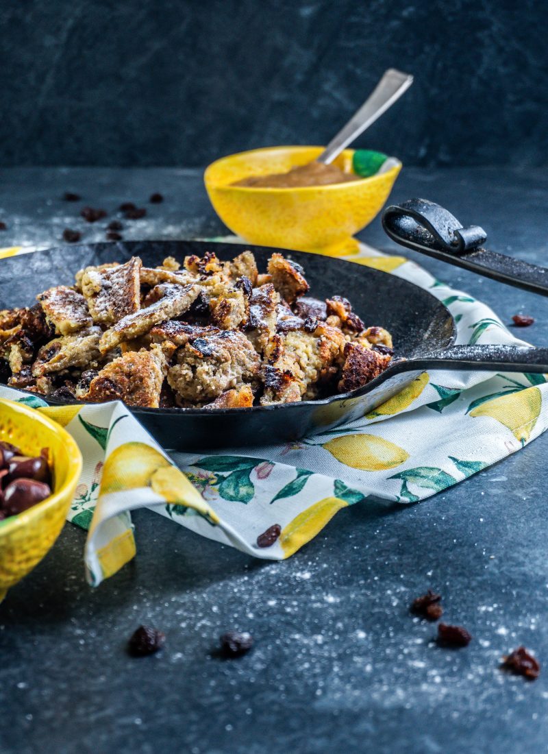 Gluten-free Kaiserschmarrn in a cast iron pan with some dusted xylitol on top and some apple sauce in the back; photographed from a side-angle
