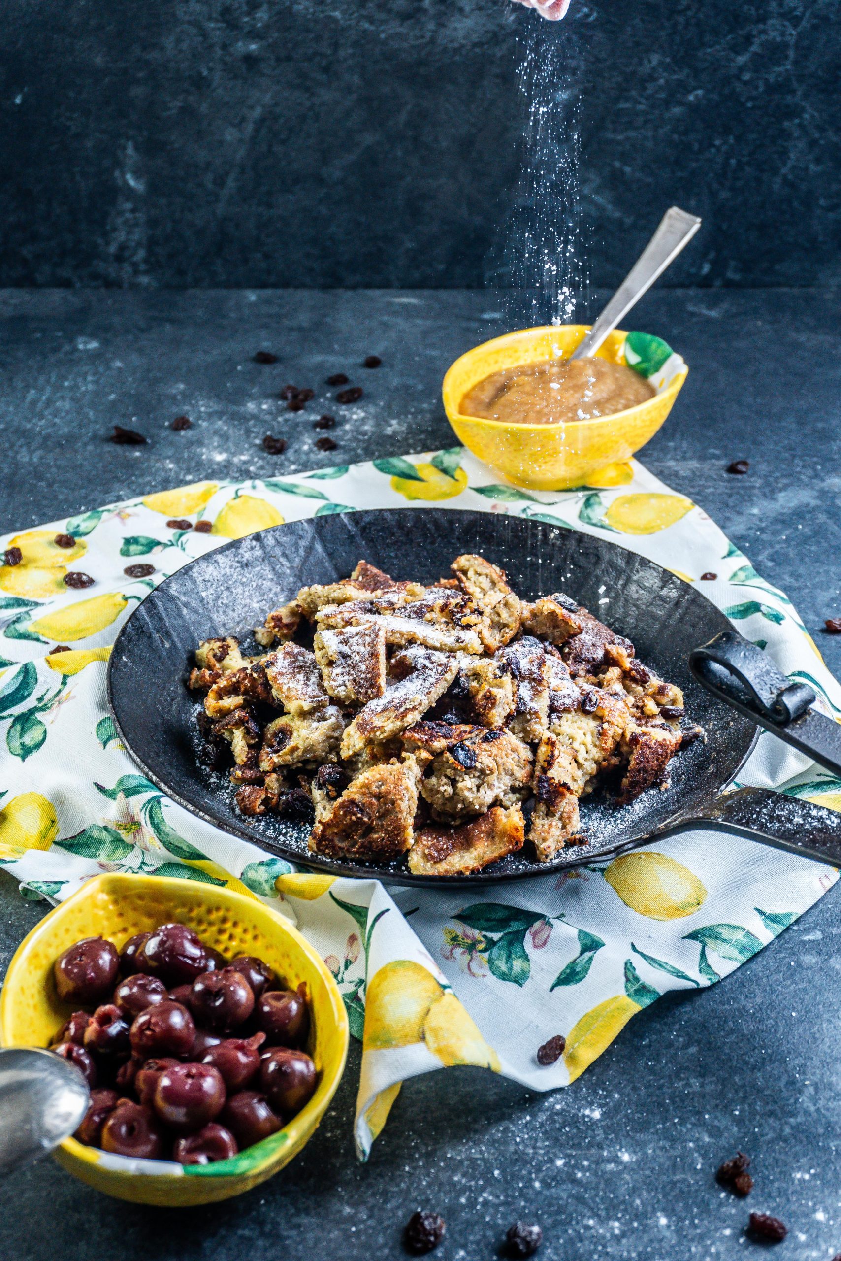 Gluten-free Kaiserschmarrn with powdered xylitol being put onto the Kaiserschmarrn and drizzle being visible
