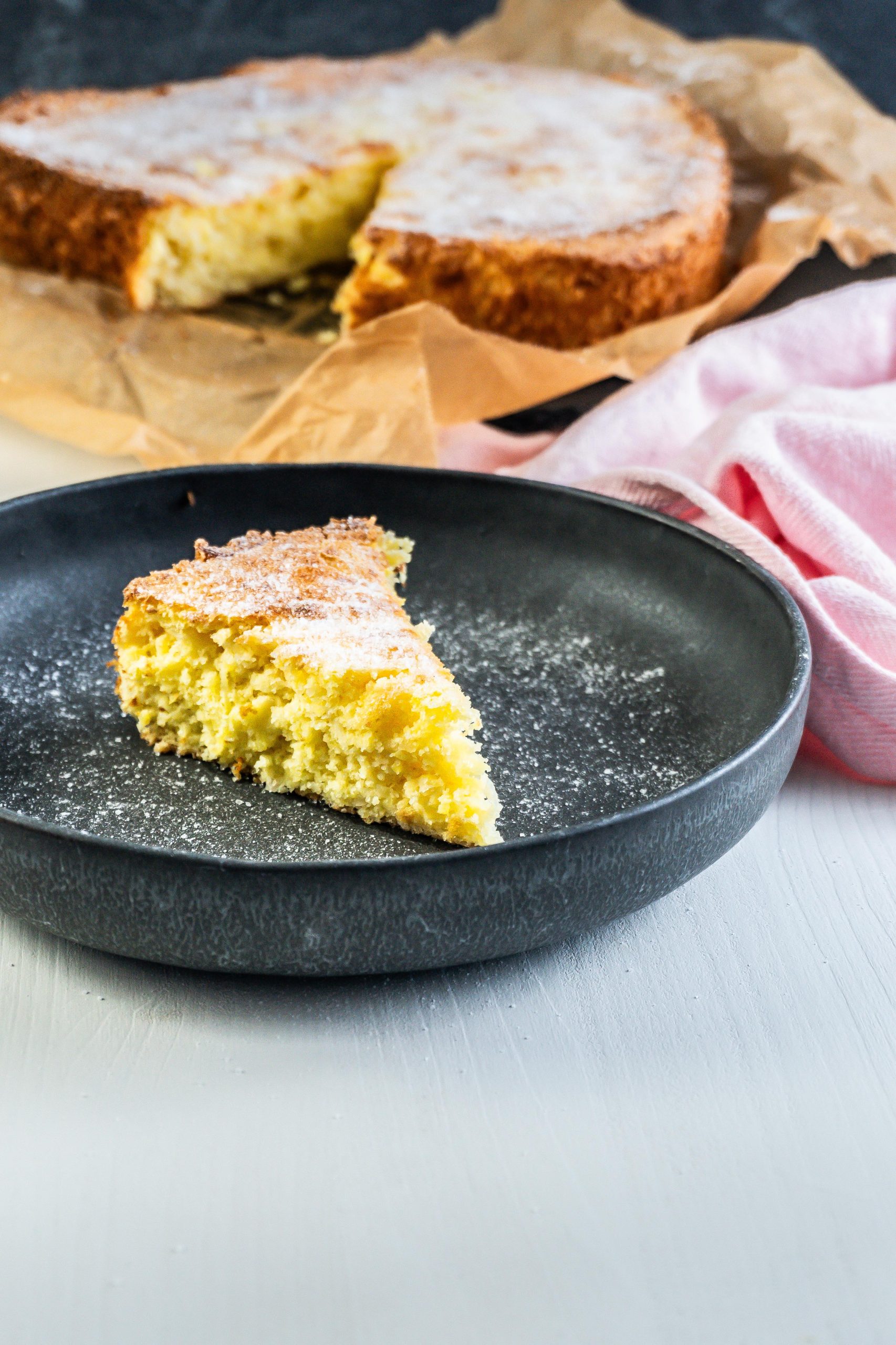 A piece of polenta pound cake is on a small plate with the larger one being visible in the background