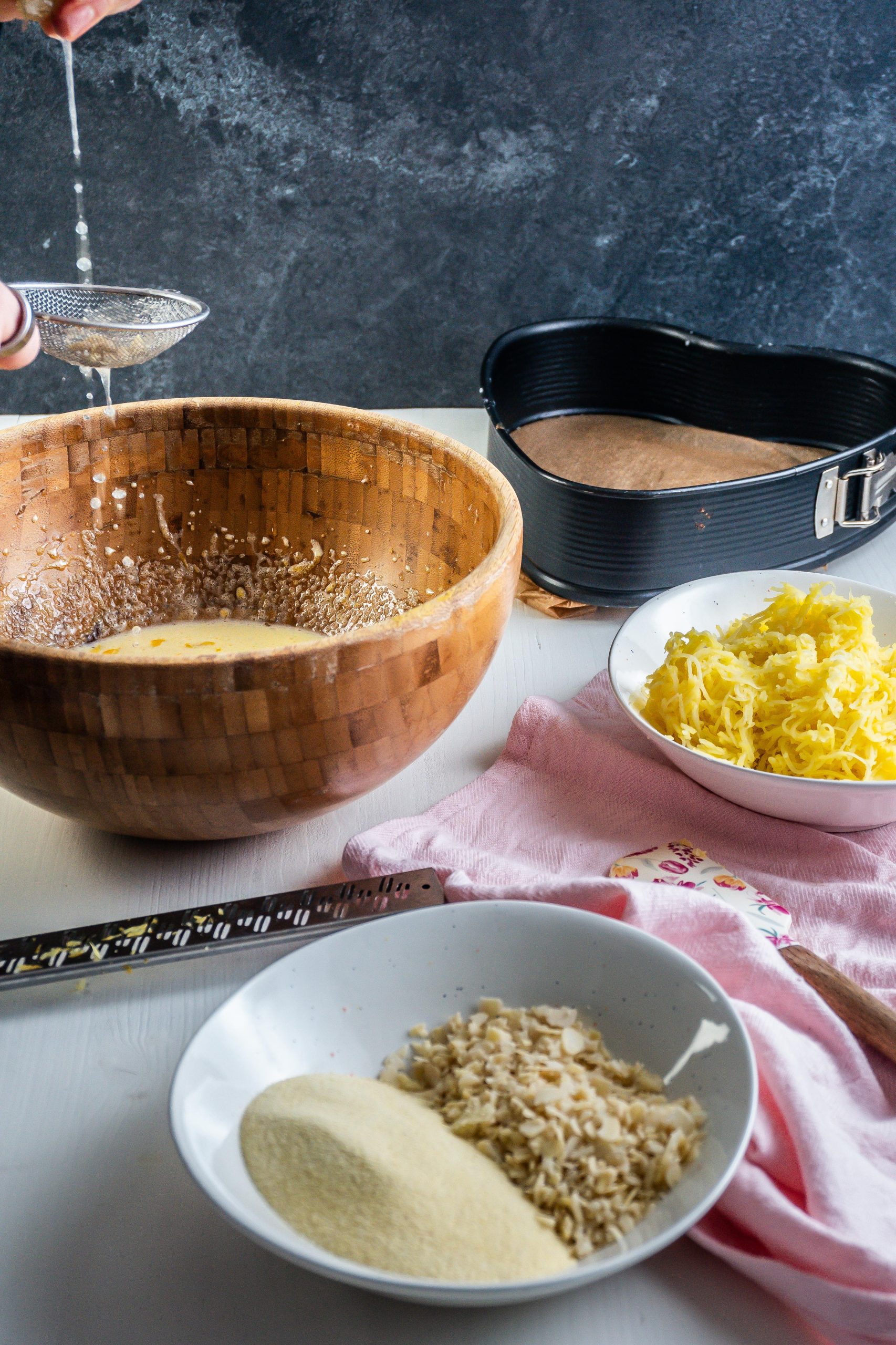 Egg yolks and xylitol being beaten in a bowl with lemon juice being added and other ingredients for the potato pound cake being scattered in the frame