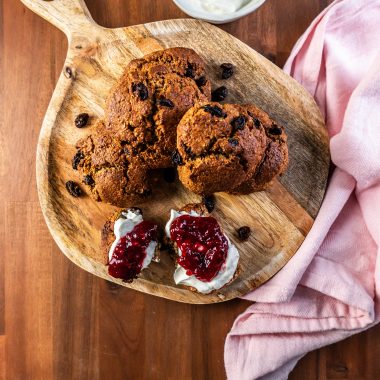 Cinnamon Orange Raisin Scones arranged on a platter with some jam and yogurt visible to the side and one scone being slathered in both