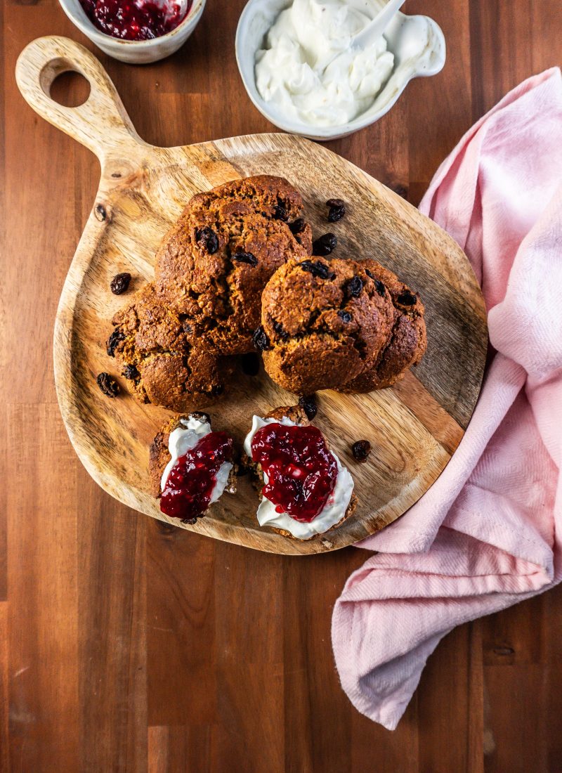 Cinnamon Orange Raisin Scones arranged on a platter with some jam and yogurt visible to the side and one scone being slathered in both