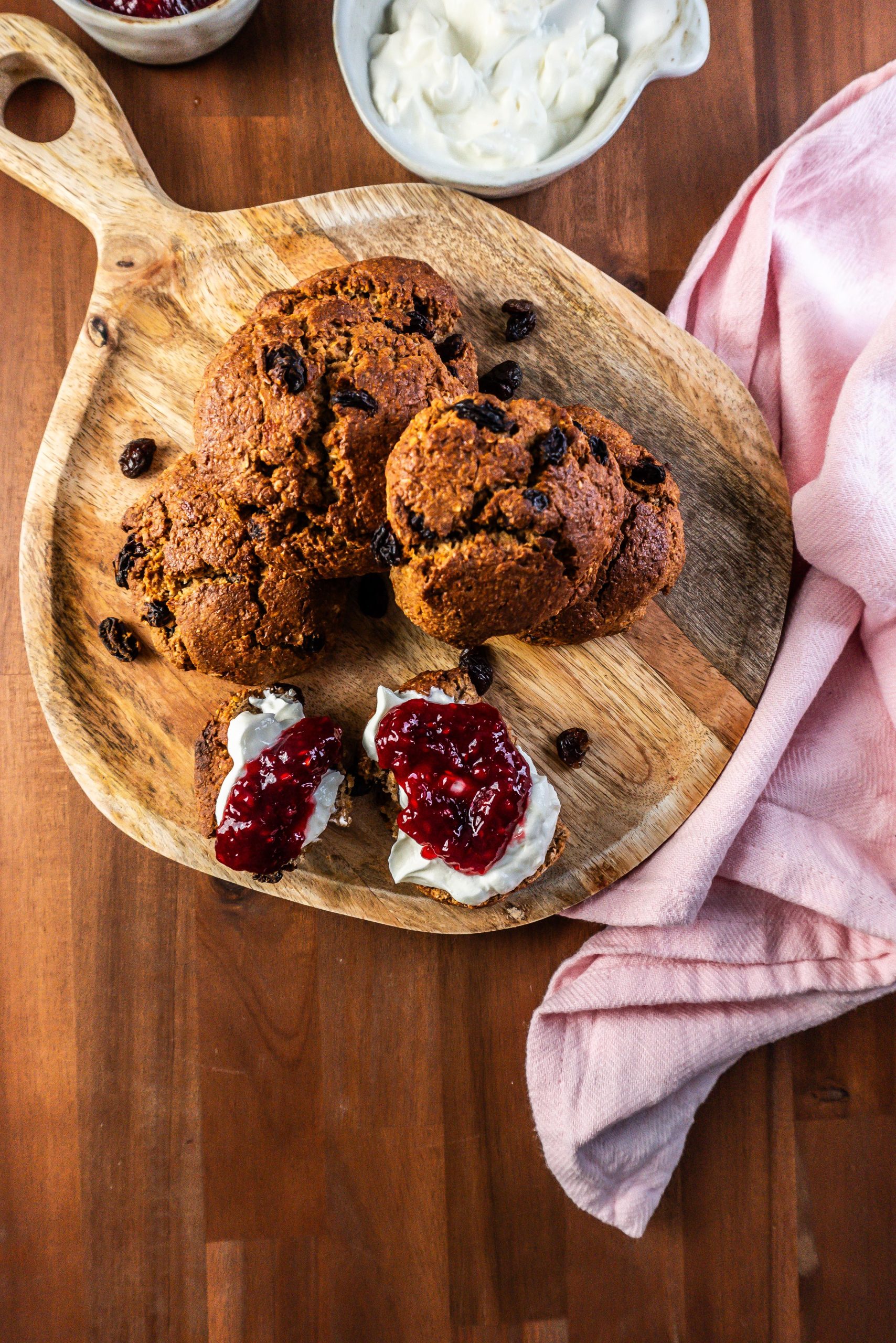 Cinnamon Orange Raisin Scones arranged on a platter with some jam and yogurt visible to the side and one scone being slathered in both