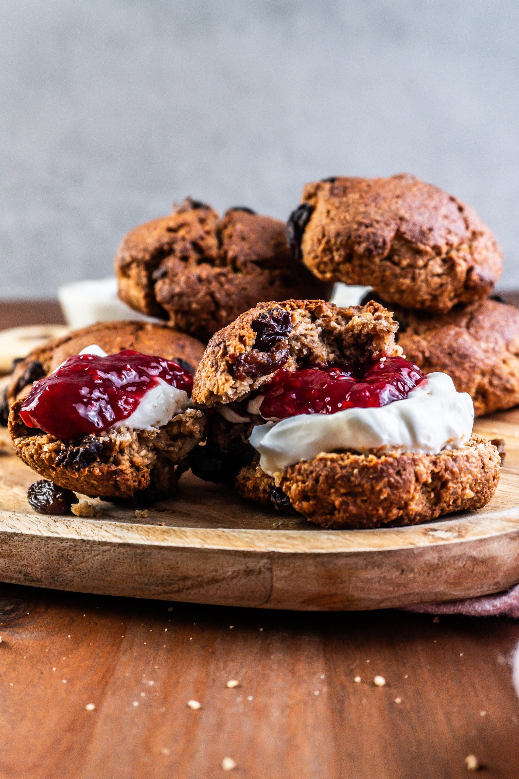 Cinnamon Orange Raisin Scones arranged on a platter with some jam and yogurt visible to the side and one scone being slathered in both; photographed up close