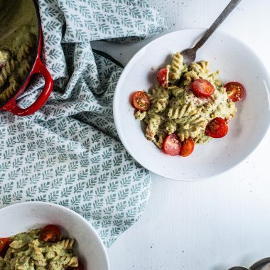 Creamy Avocado Pasta Recipe plated in two bowls with a fork stuck into one, with the casserole dish that the pasta was made in visible to the side