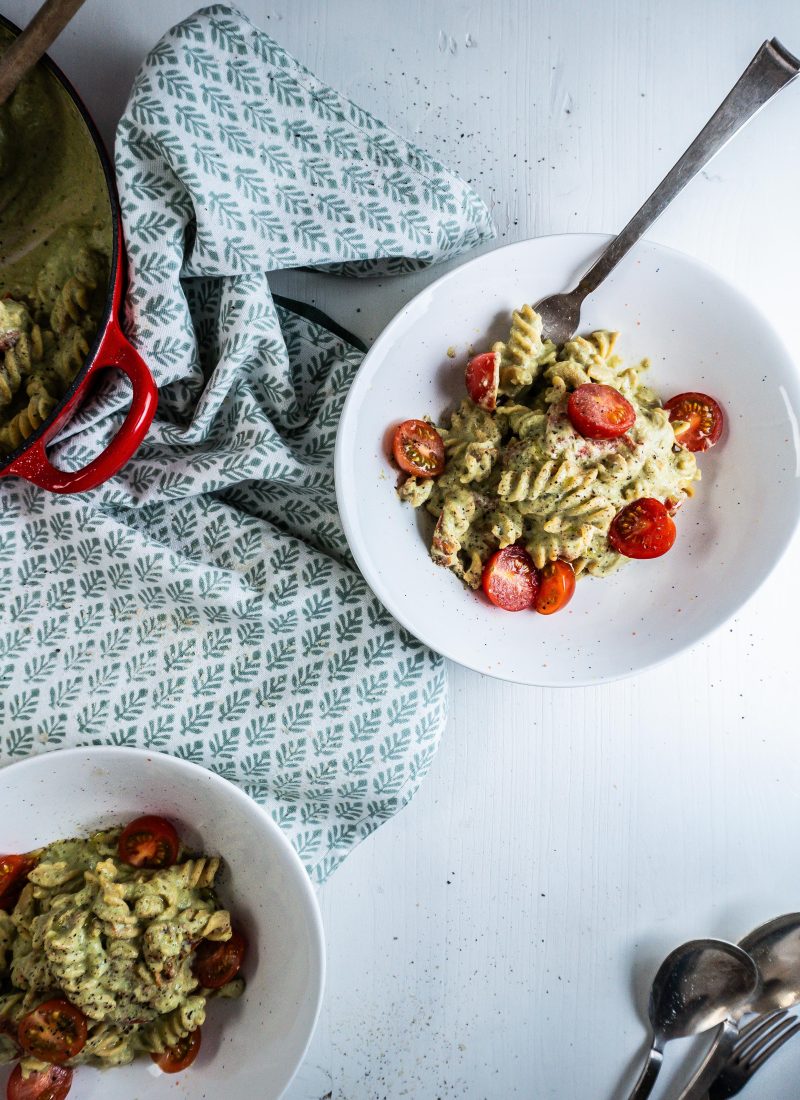 Creamy Avocado Pasta Recipe plated in two bowls with a fork stuck into one, with the casserole dish that the pasta was made in visible to the side