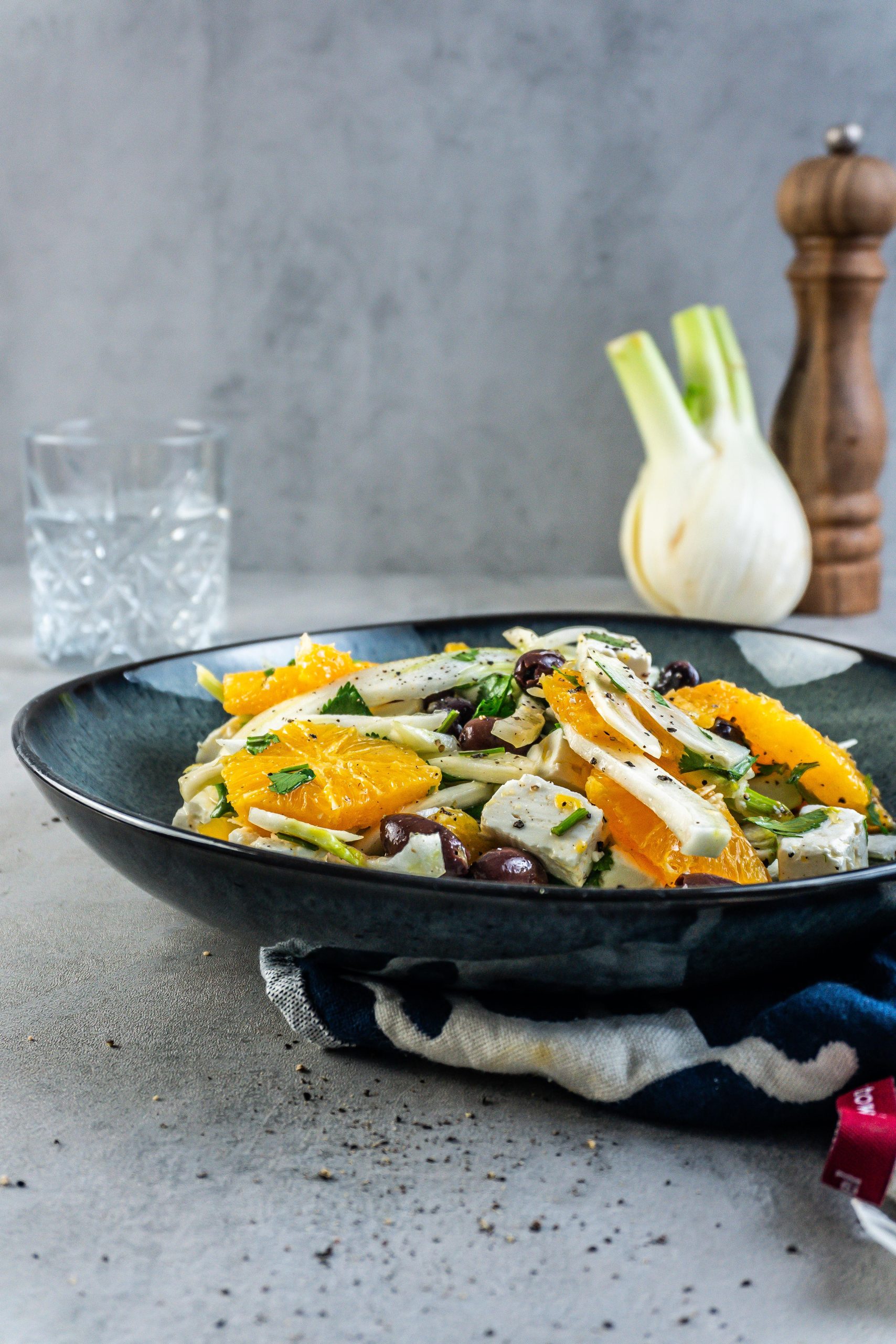 Mediterranean Fennel and Orange Salad on a dark plate with a glass of water and fennel visible in the background