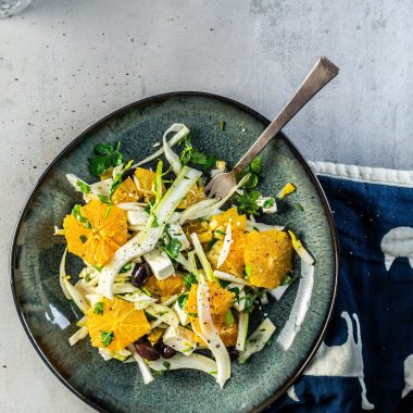 Mediterranean Fennel and Orange Salad on a dark plate with a fork tugged into it and a dish towel stuck under the plate