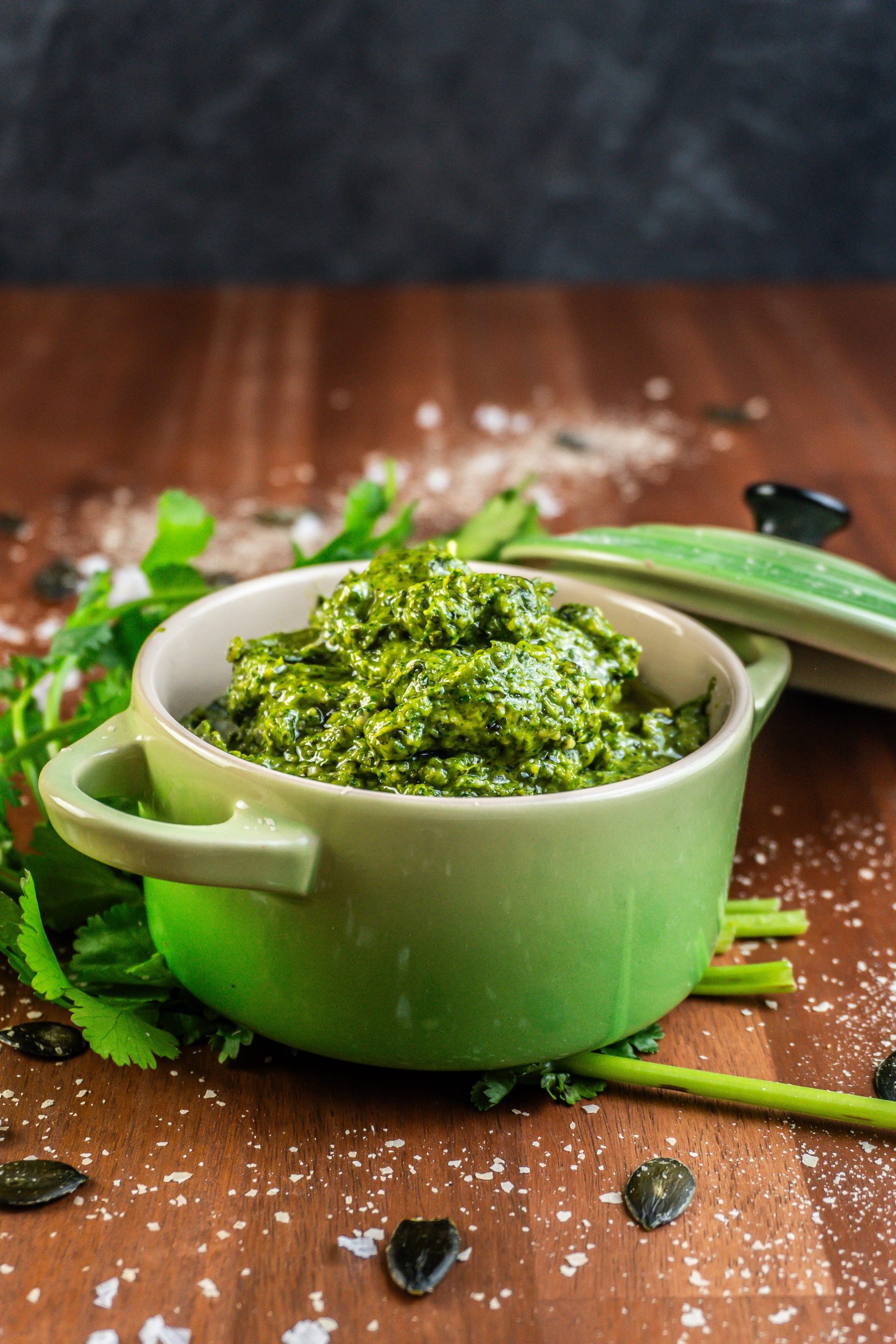 Five Minute Vegan Pepita Cilantro Pesto in a small ramekin dish with some cilantro, pepitas, and nutritional yeast scattered around
