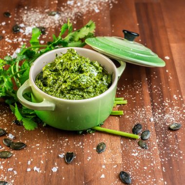 Five Minute Vegan Pepita Cilantro Pesto in a small ramekin dish with some cilantro, pepitas, and nutritional yeast scattered around