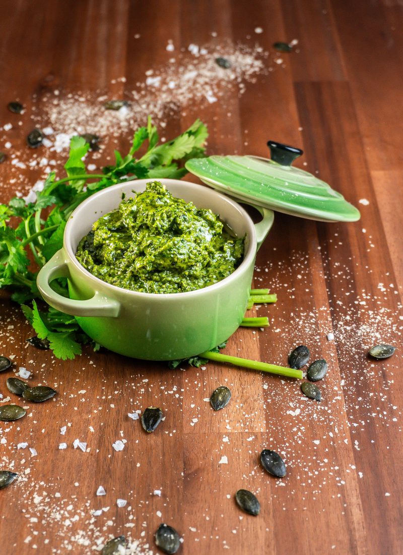 Five Minute Vegan Pepita Cilantro Pesto in a small ramekin dish with some cilantro, pepitas, and nutritional yeast scattered around
