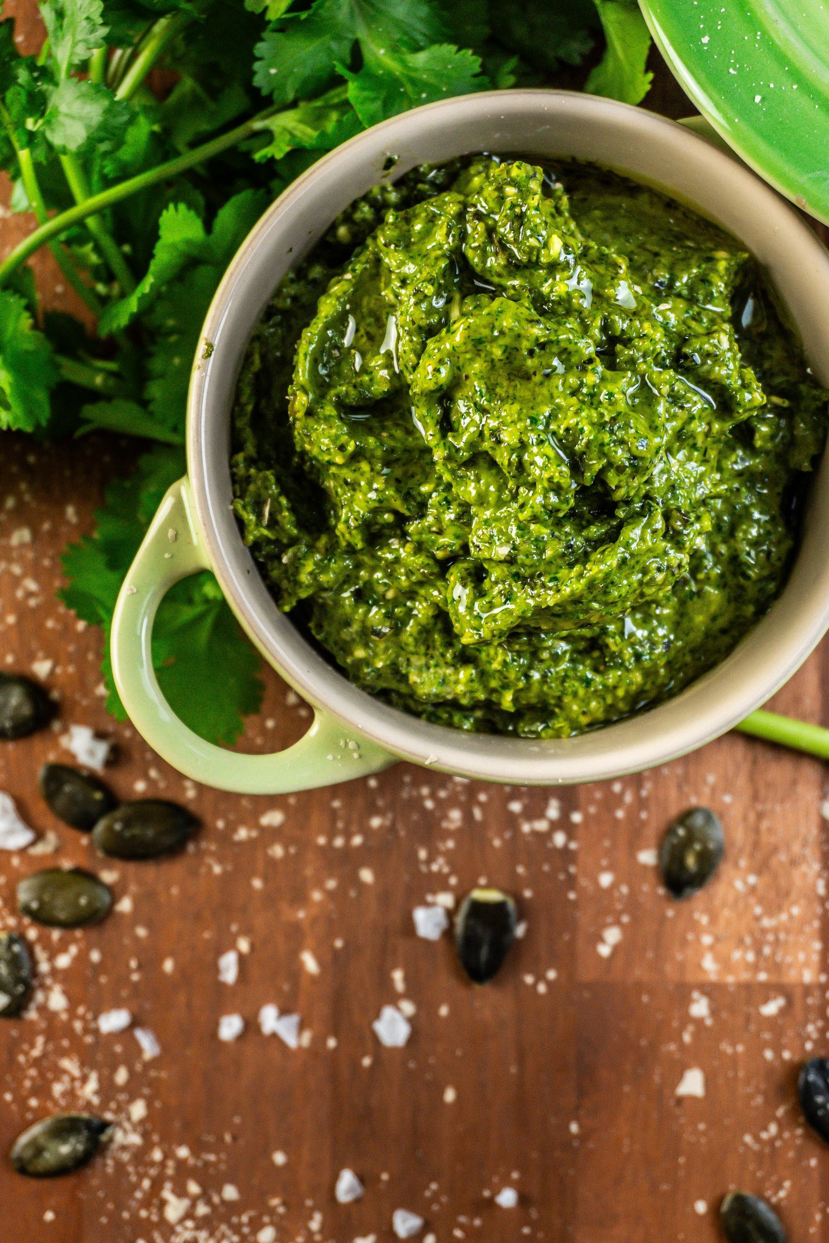 Five Minute Vegan Pepita Cilantro Pesto in a small ramekin dish with some cilantro, pepitas, and nutritional yeast scattered around; photographed from above