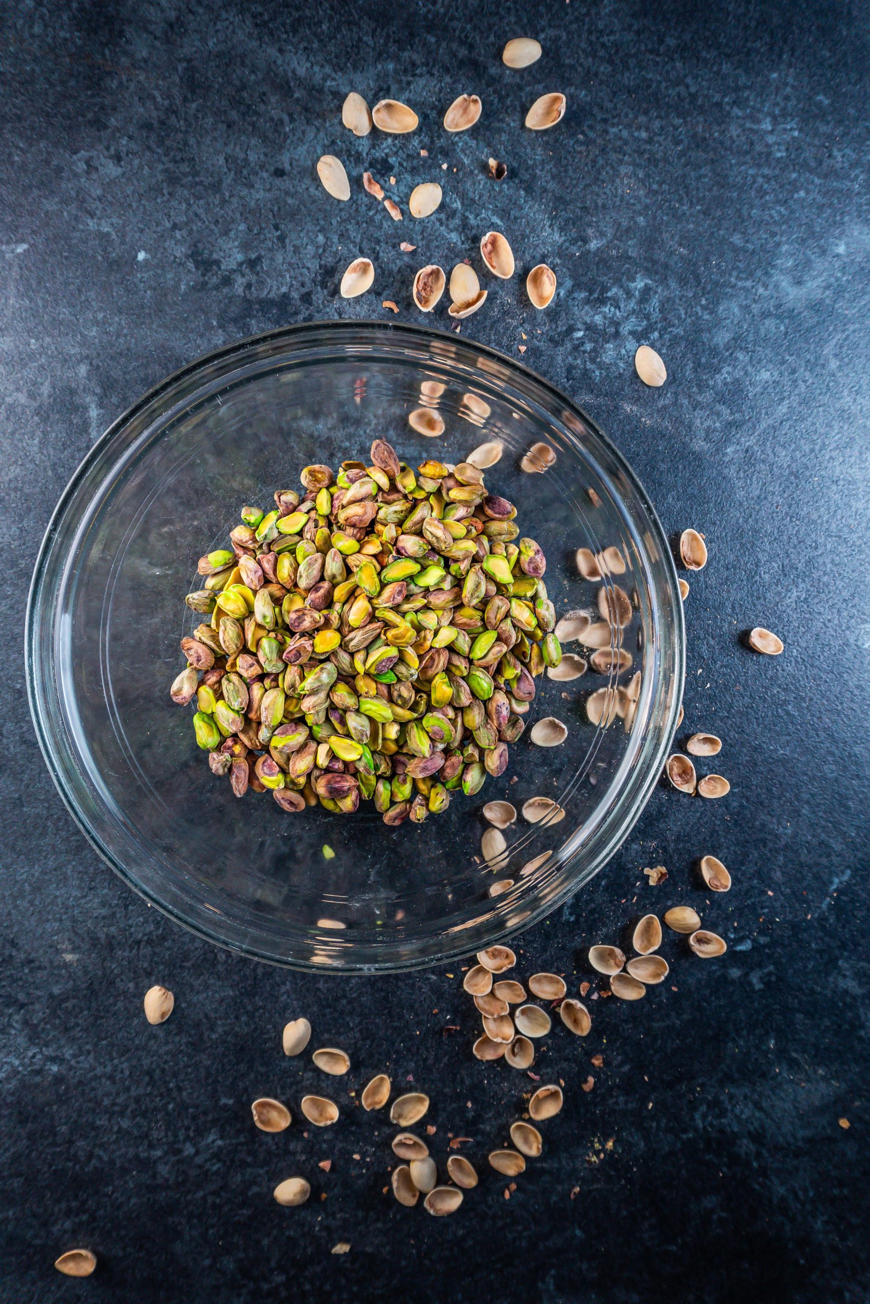 Pistachios in a glass dish with some shells scattered around