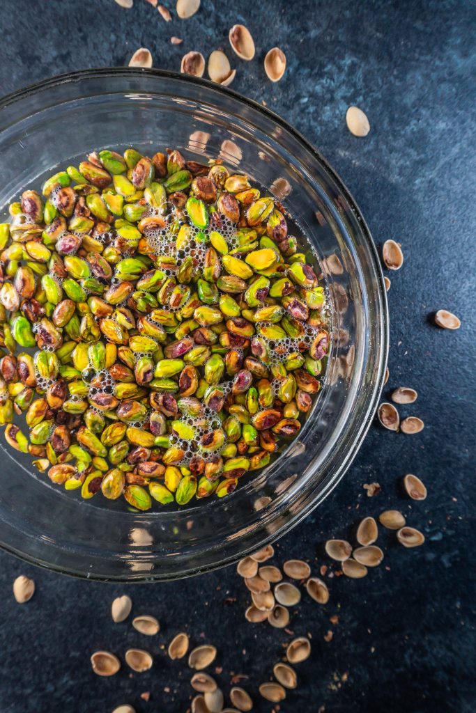 Pistachios in a glass dish covered in boiling water with some shells scattered around