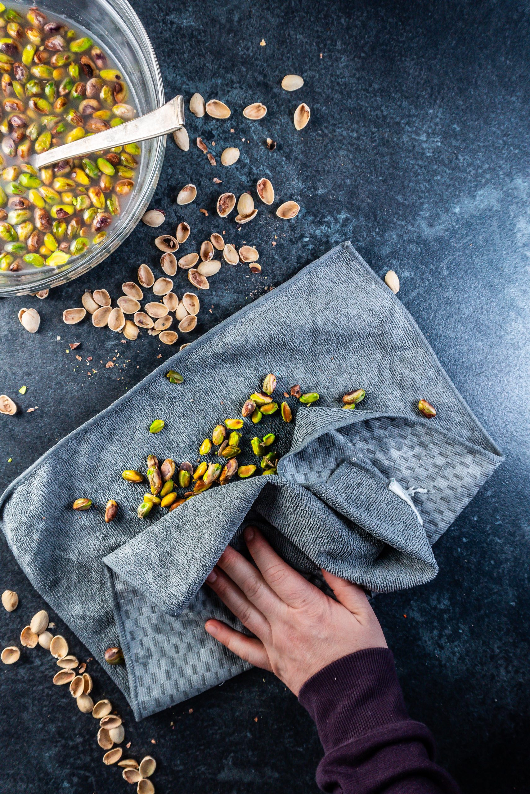 Boiled pistachios in a towel being rubbed free of their outer "skin"