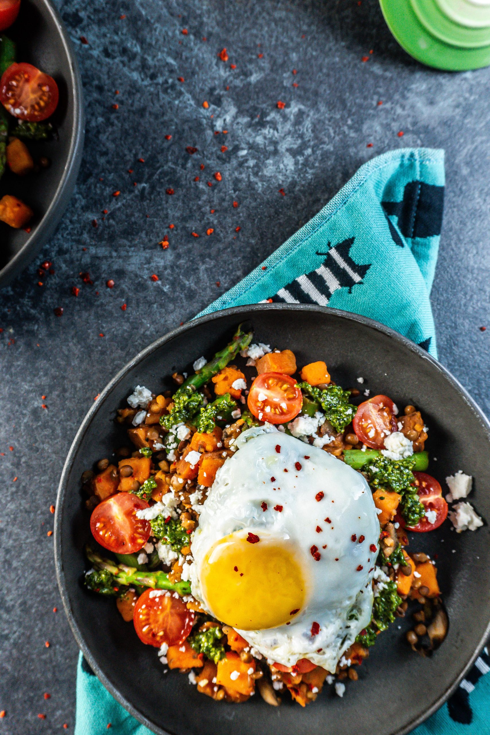 Savory Breakfast Bowl with a sunny upside egg plated in a dark bowl and some chili flakes scattered around; photographed from above