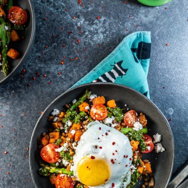 Savory Breakfast Bowl with a sunny upside egg plated in a dark bowl and some chili flakes scattered around; photographed from above
