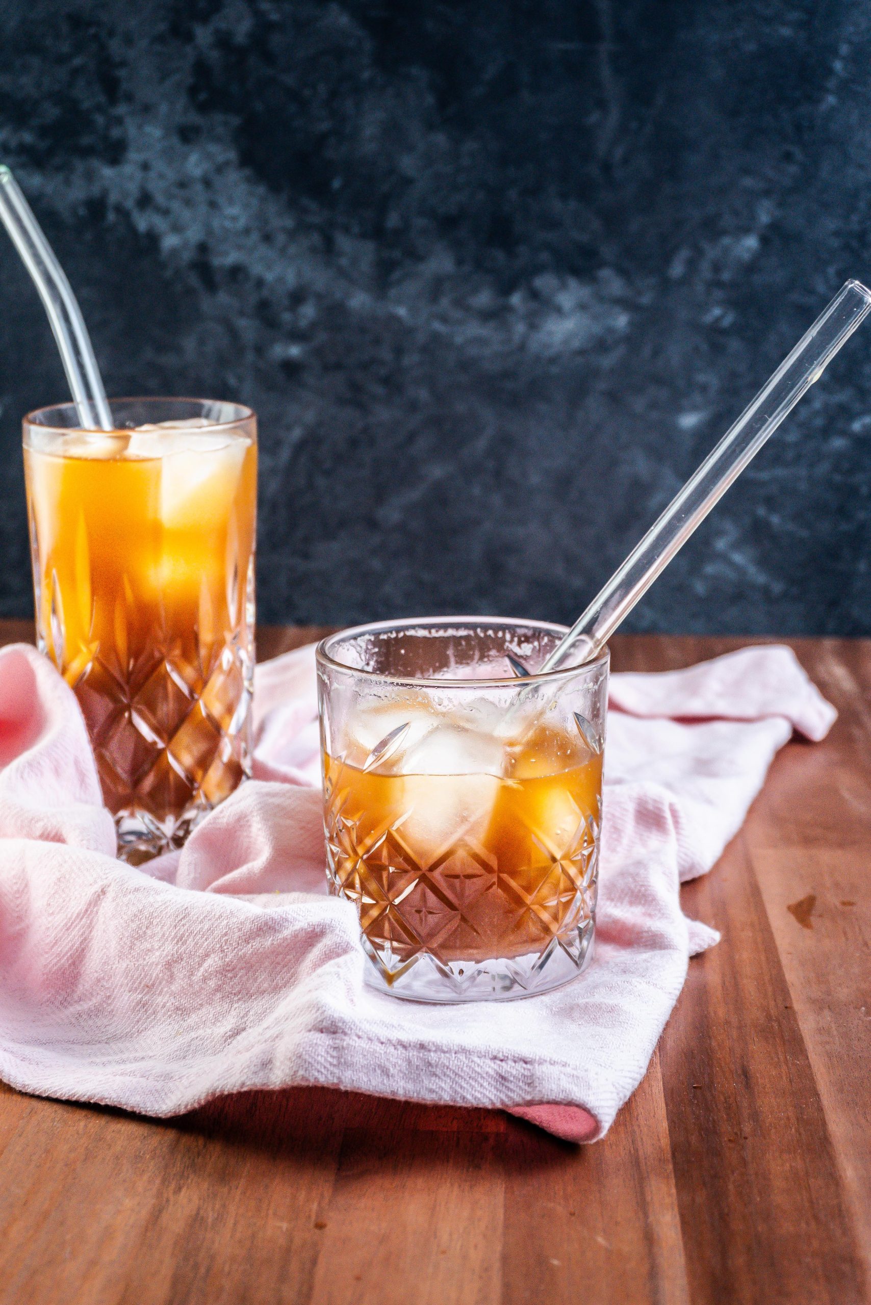 Coffee Ginger Elixir in a glass with a straw being half drunk, another glass visible in the background on a kitchen towel