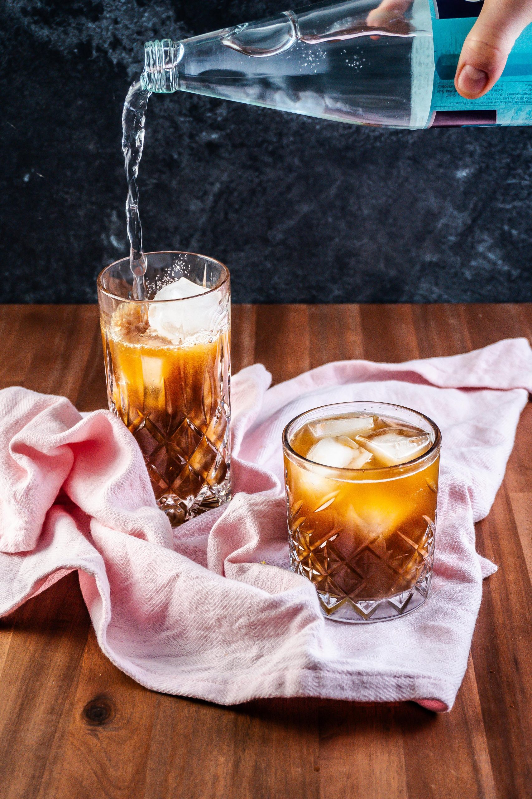 Coffee Ginger Elixir in the making with coffee, ginger, and maple syrup already in the glass with mineral water being added to a second glass