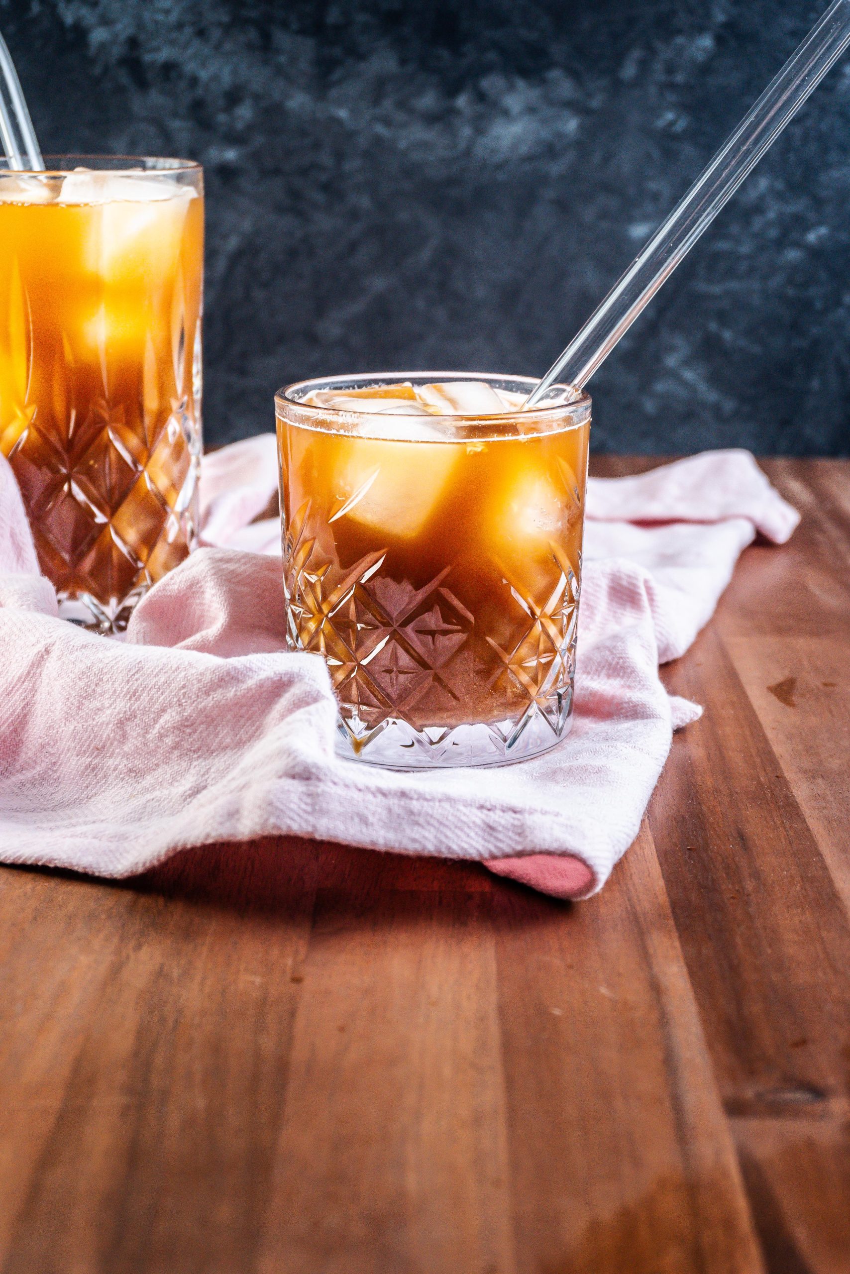Coffee Ginger Elixir in a glass with a straw, another glass visible in the background on a kitchen towel