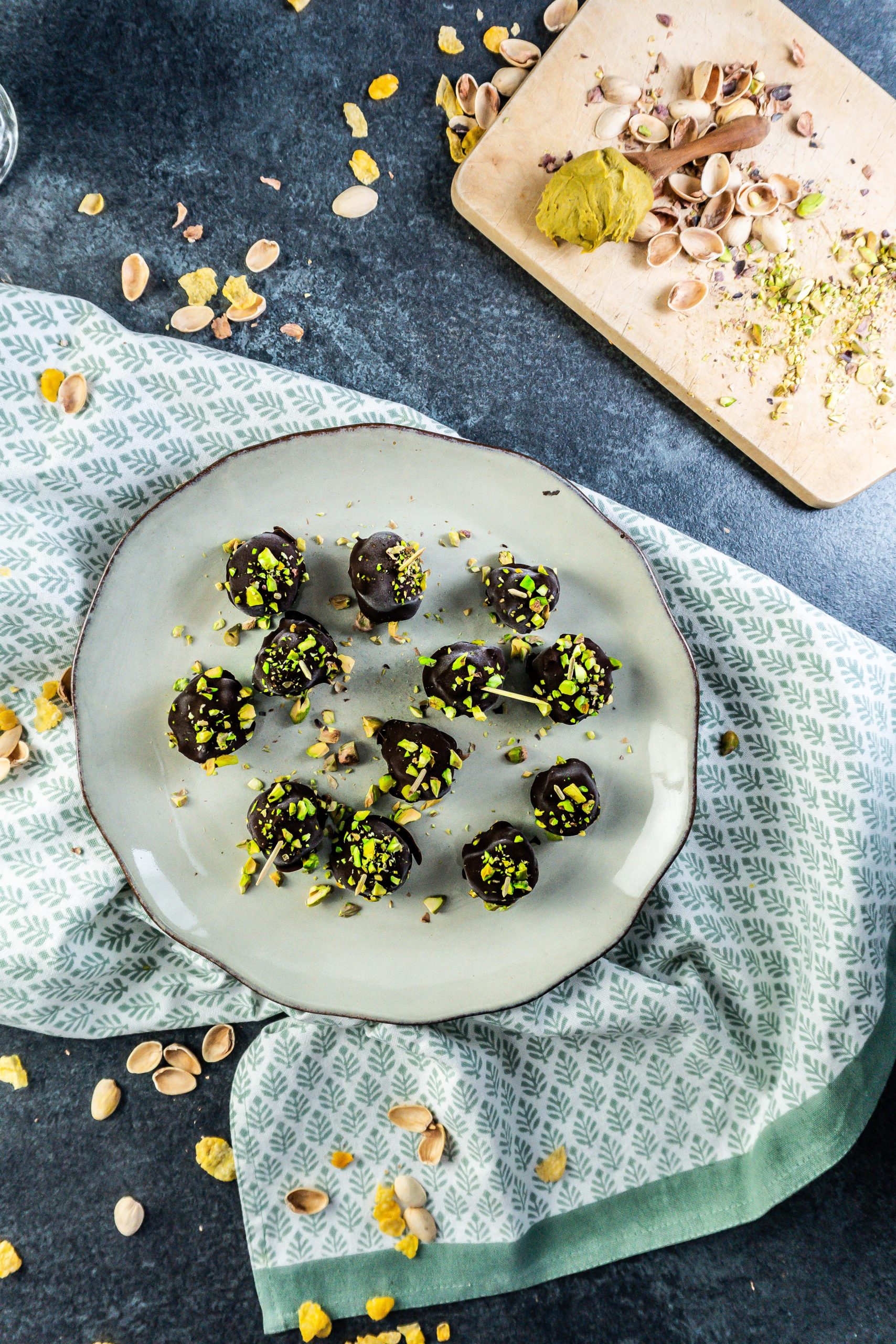Gluten-free Dubai Style Pistachip Balls on a plate with some chopped pistachios strewn on top and some strewn pistachio shells framing the picture