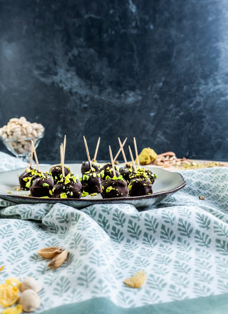 Gluten-free Dubai Style Pistachip Balls on a plate with some chopped pistachios strewn on top and some pistachios in a glass jar visible in the background