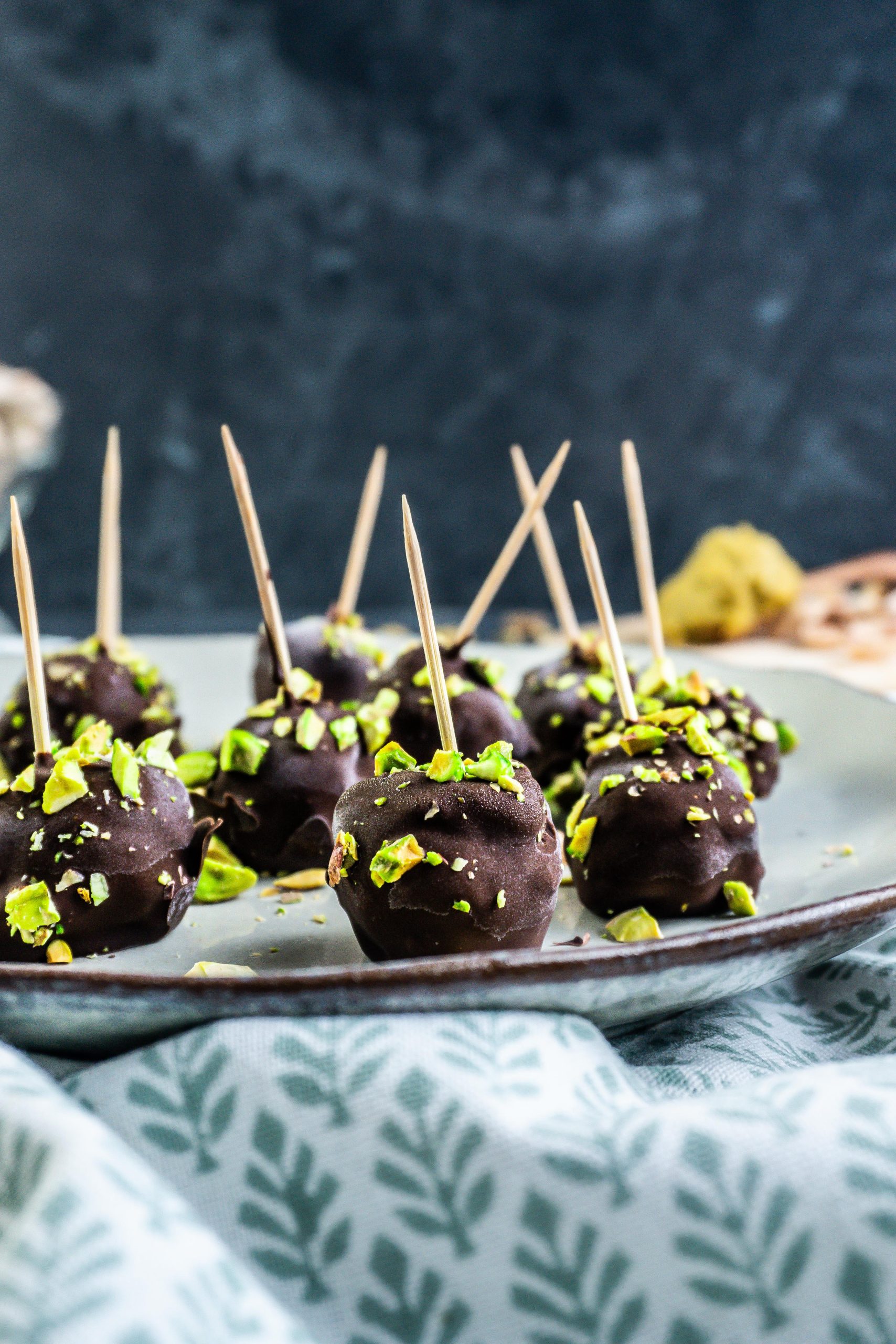 Gluten-free Dubai Style Pistachip Balls on a plate with some chopped pistachios strewn on top; photographed from a side-angle