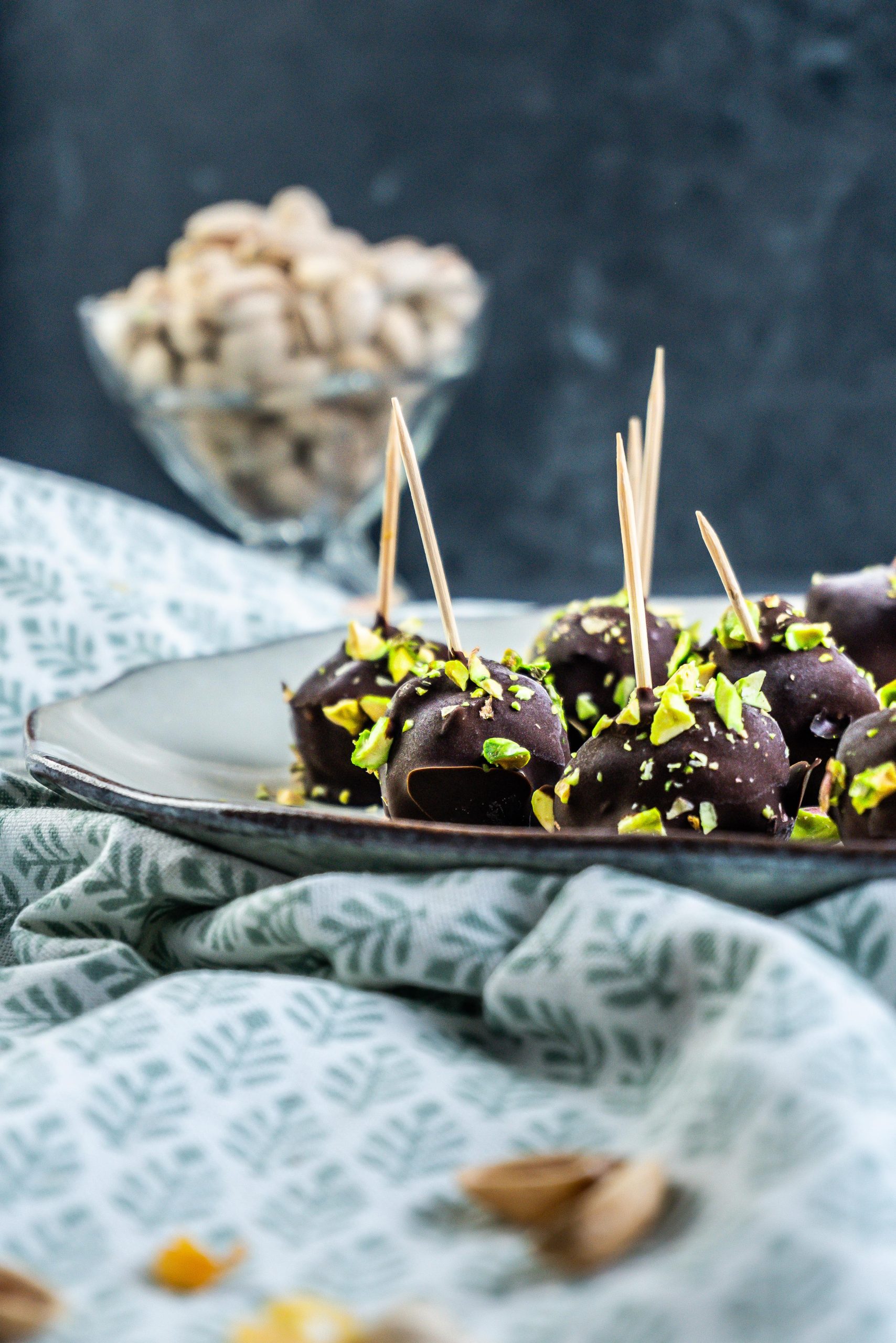 Gluten-free Dubai Style Pistachio Balls on a plate with some chopped pistachios strewn on top and pistachios visible in the background