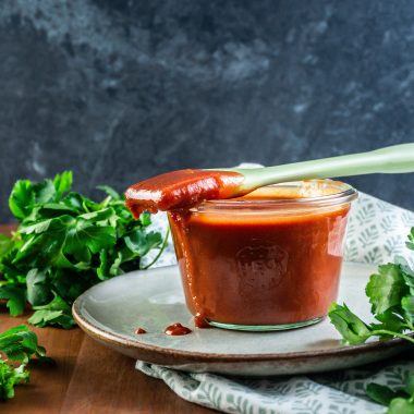 Homemade BBQ Sauce in a glass jar with a spoon dipped into the sauce and laying on the rim of the glass jar