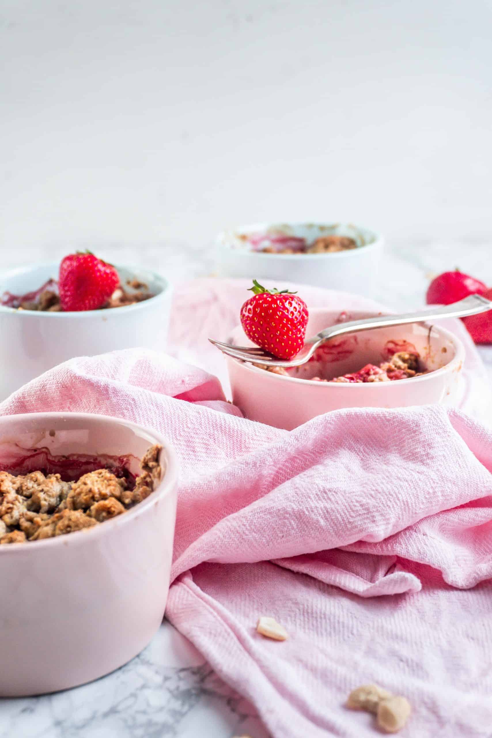 Strawberry Rhubarb Crumble with a fork laying on the ramekin and a strawberry balancing on it