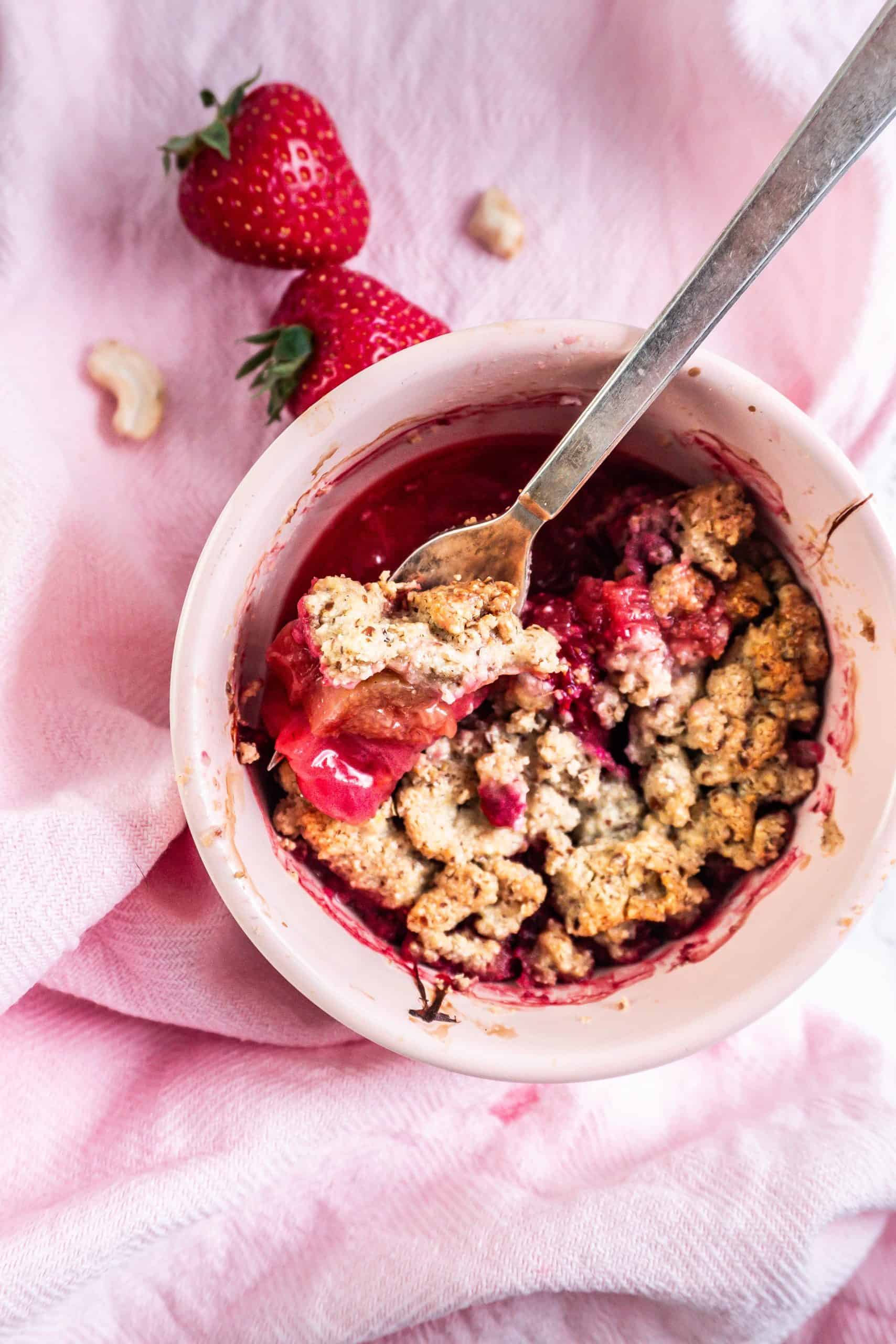 Strawberry Rhubarb crumble in a ramkin with a fork tugging into the crumble, photographed up close