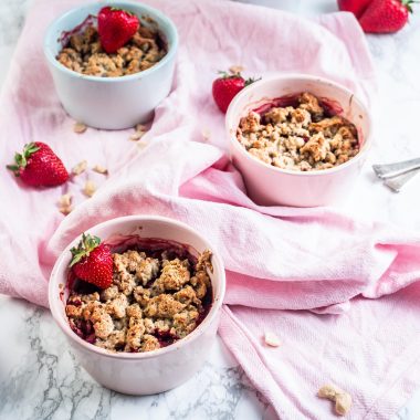 Strawberry Rhubarb Crumble in small ramekins with strawberries and cashews strewn around